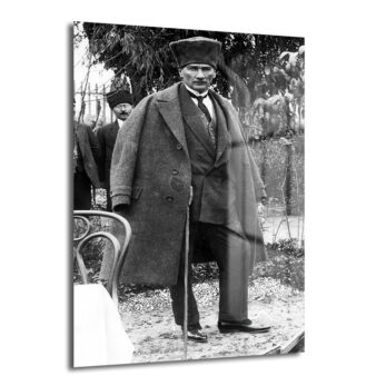 Mustafa Kemal Atatürk'ün şapkalı, pardösülü ve bastonlu olarak bahçede çekilmiş, arkasında bir başka kişinin de göründüğü siyah beyaz, tarihi bir fotoğrafı.